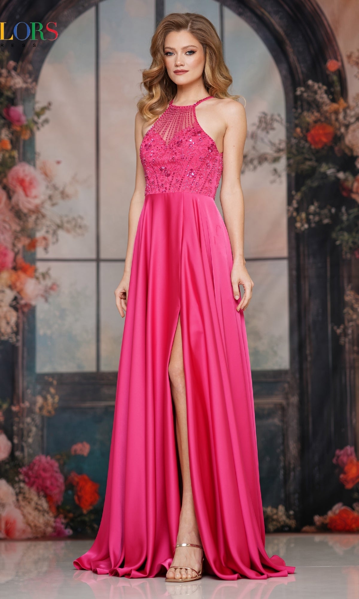 Wearing the Colors Dress 3822 High-Neck Halter Prom Gown, a woman stands before a floral arched window, her loose waves and nude heels enhancing the beaded bodice and thigh-high slit of this bold pink formal dress.